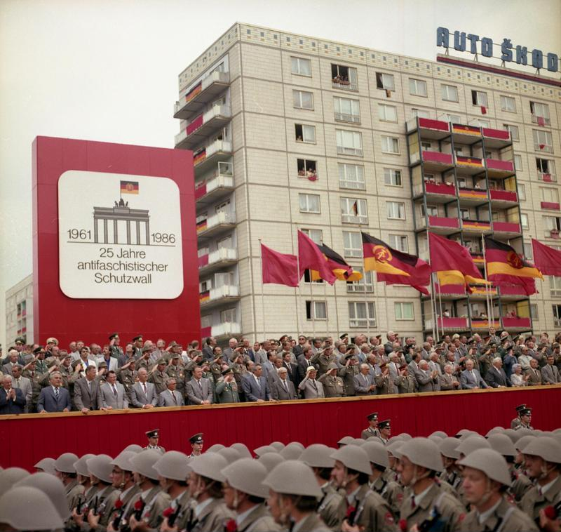 Photo of a GDR military parade with all the political elite gathered on a stage. 
Sing in the background says 25 years of anti fascist protection wall. 
The image is a link to the original source of it. 
